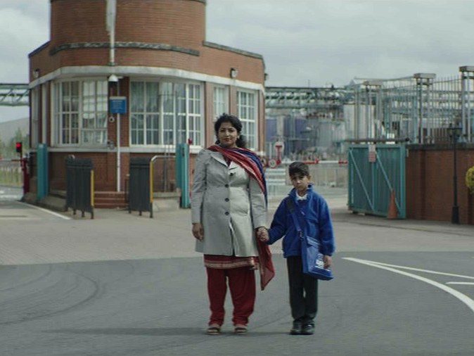 Indi: a mother and child crossing a Black Country street, the factory gatehouse behind them.