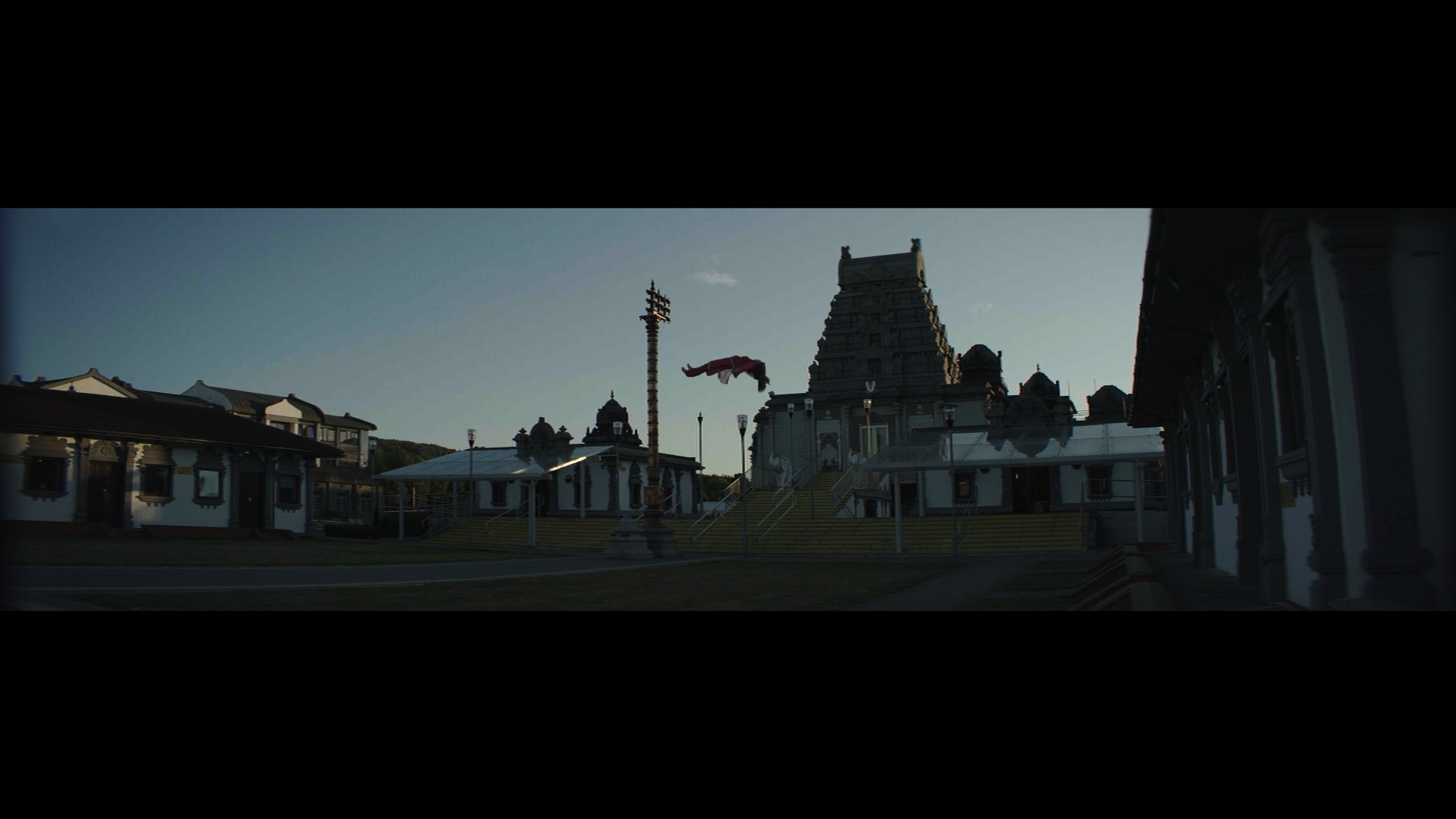 Indi film still: Hindu temple at dusk, a flag flying from the gopuram, the sky turning cold blue.