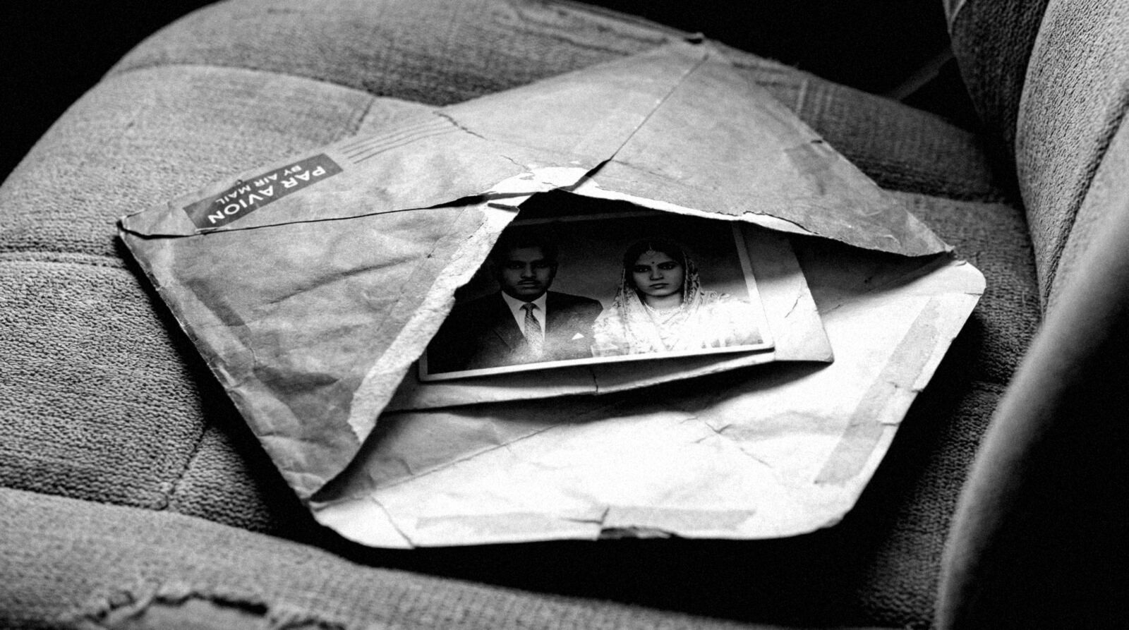 Year Zero: Black Country, archival still: a torn par avion air mail envelope opened across a sofa, a black-and-white wedding photograph slipping out.